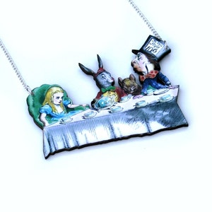 May include: A wooden necklace depicting a scene from Alice in Wonderland. The Mad Hatter, the March Hare, Alice, and the Dormouse are seated at a table having tea. The necklace is painted in bright colours and features a silver chain.