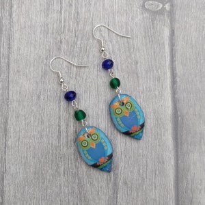 May include: A pair of owl earrings with blue and green glass beads. The owls are blue with yellow and green accents.