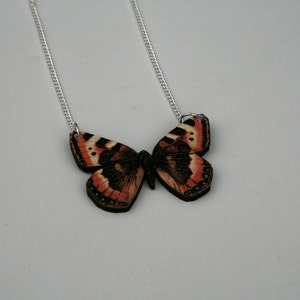 May include: A silver chain necklace with a wooden butterfly pendant. The butterfly is painted with realistic details in shades of brown, orange, and black.