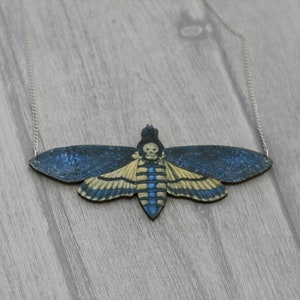 May include: A silver chain necklace with a wooden pendant shaped like a blue and yellow moth with a skull design.
