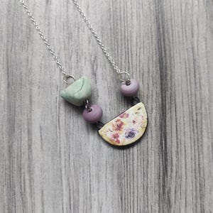 May include: A silver chain necklace with a floral patterned half-circle pendant, a green bird-shaped bead, and two purple beads.