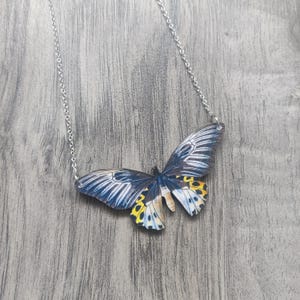 May include: A silver chain necklace with a large, blue, yellow, and white butterfly pendant.