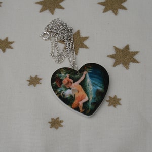 May include: Heart-shaped pendant necklace with a silver chain. The pendant features a vintage illustration of a woman in a flowing dress. The background is a white surface with gold star patterns.