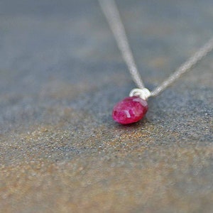May include: A delicate silver chain necklace with a single, faceted, ruby red gemstone pendant.