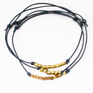 May include: A layered bracelet with three strands of dark blue cord and gold-toned metal beads. The beads are hexagonal in shape and are arranged in a row on each strand.