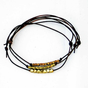 May include: A brown leather bracelet with a row of gold-toned metal beads.