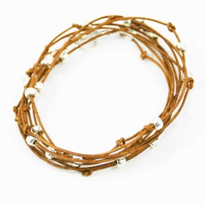 May include: A brown leather wrap bracelet with silver beads. The bracelet is made of multiple strands of leather that are woven together.