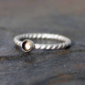 May include: A silver ring with a twisted band and a small, round, brown gemstone.