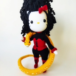 May include: Crochet pattern PDF in English for a Hello Kitty amigurumi doll with black curly hair, a red bodice, black pants, and a yellow snake.
