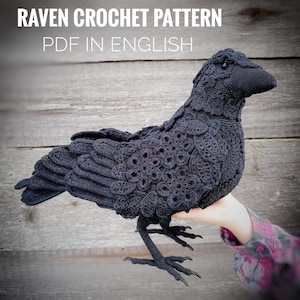 Könnte beinhalten: Ein dunkelgrauer Häkelrabe mit detaillierten Feder- und Flügelmustern. Der Vogel sitzt auf einer Hand und zeigt sein kompliziertes Design. Der Text auf dem Bild lautet "Raven Crochet Pattern PDF in English."