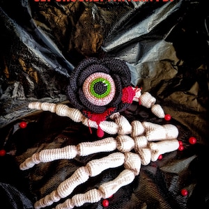 Op de afbeelding: Gehaakte Halloween-set met een zwarte roos met een oog, een skelet hand en rode accenten. De tekst "SET CROCHET PATTERN PDF" staat bovenaan. Het ontwerp staat tegen een donkere, getextureerde achtergrond.