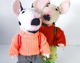 May include: Two crocheted Bull Terrier dolls. One doll wears a peach sweater, gray pants, and pink shoes. The other doll wears an orange sweater and green pants. The text "CROCHET PATTERN PDF IN ENGLISH" and "BULL TERRIER" are visible.