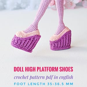 May include: Crocheted doll legs wearing light pink and purple high platform shoes. Text reads: DOLL HIGH PLATFORM SHOES, crochet pattern pdf in english, FOOT LENGTH 35-36.5 MM. The shoes feature a thick, textured purple sole and a light pink upper.