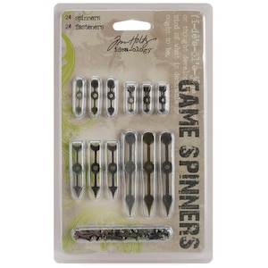 May include: A package of 24 metal game spinners and 24 fasteners. The spinners are black and gold and have a pointed arrow shape. The fasteners are small and silver. The package is labeled "Game Spinners" and "Idea-ology".