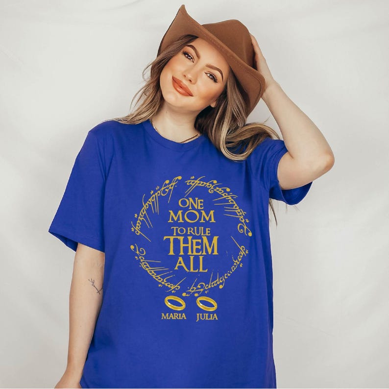 May include: A royal blue t-shirt with gold lettering that reads "ONE MOM TO RULE THEM ALL" in a circular design. Below the text are two gold rings and the names "MARIA JULIA".