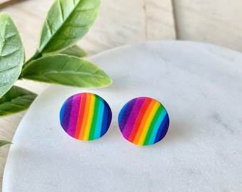 Op de afbeelding: Twee ronde oorstekers met een regenboogstreepmotief. De oorbellen tonen een spectrum aan kleuren, waaronder rood, oranje, geel, groen, blauw en paars. Ze liggen op een wit marmeren oppervlak.