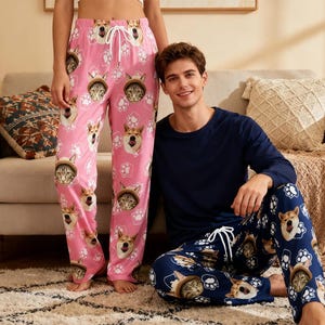 Könnte beinhalten: Rosa Schlafanzughose mit einem sich wiederholenden Muster aus Shiba Inu-Hunden und Katzen mit Hüten. Die Hose hat einen Kordelzug in der Taille. Eine Person trägt die rosa Hose. Eine andere Person trägt eine marineblaue Schlafanzughose mit einem ähnlichen Muster.