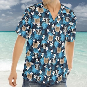 Puede incluir: Una camisa de manga corta con estampado azul y blanco con una variedad de caras de animales, incluyendo gatos y perros. La camisa tiene un cuello abotonado y un ajuste holgado.