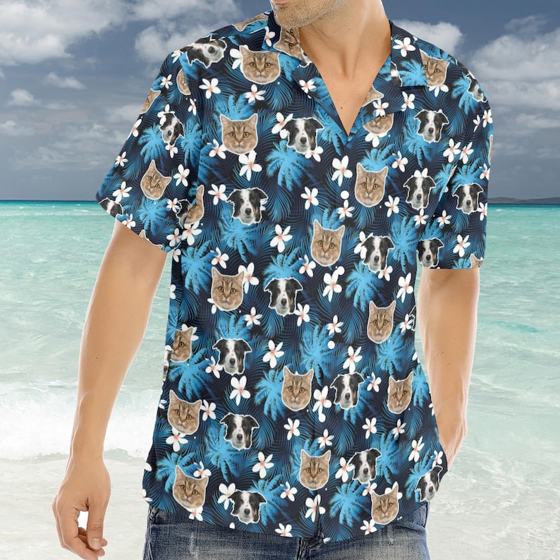 Puede incluir: Una camisa de manga corta con estampado azul y blanco con una variedad de caras de animales, incluyendo gatos y perros. La camisa tiene un cuello abotonado y un ajuste holgado.