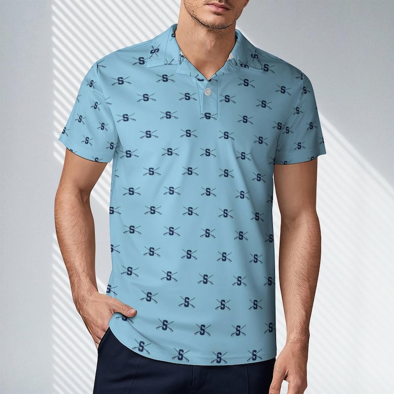 May include: Light blue polo shirt with a repeating pattern of the letter "S" and crossed hockey sticks. The shirt has a collared neckline and short sleeves. The shirt is made of a lightweight material.