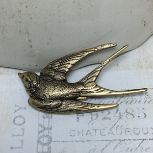 May include: A detailed, antique-style brass bird figurine with outstretched wings. The bird is a swallow, with intricate feather detailing and a textured surface. The figurine is set against a vintage-style background, suggesting a focus on decorative items.