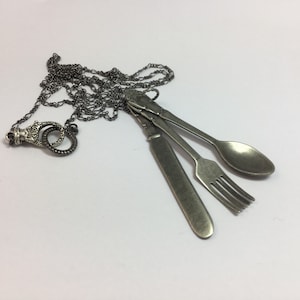 May include: A silver necklace with a pendant featuring a knife, fork, and spoon. The chain is made of small, linked circles.