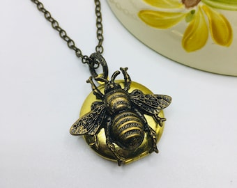 May include: A gold-toned bee locket necklace. The bee is detailed with a striped body and wings. The locket is round and has a hinged opening.