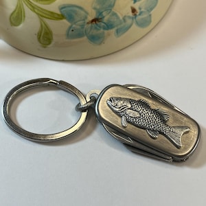 May include: A silver keychain with a multi-tool featuring a fish design. The keychain has a silver ring.