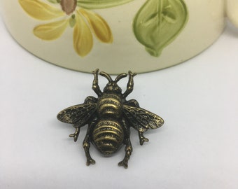 May include: A bronze-colored bee brooch with detailed wings and a textured body.