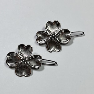 May include: Two silver-toned hair barrettes. Each barrette features a four-petal flower design with a cluster of small beads at the center. The barrettes are on a light gray background.
