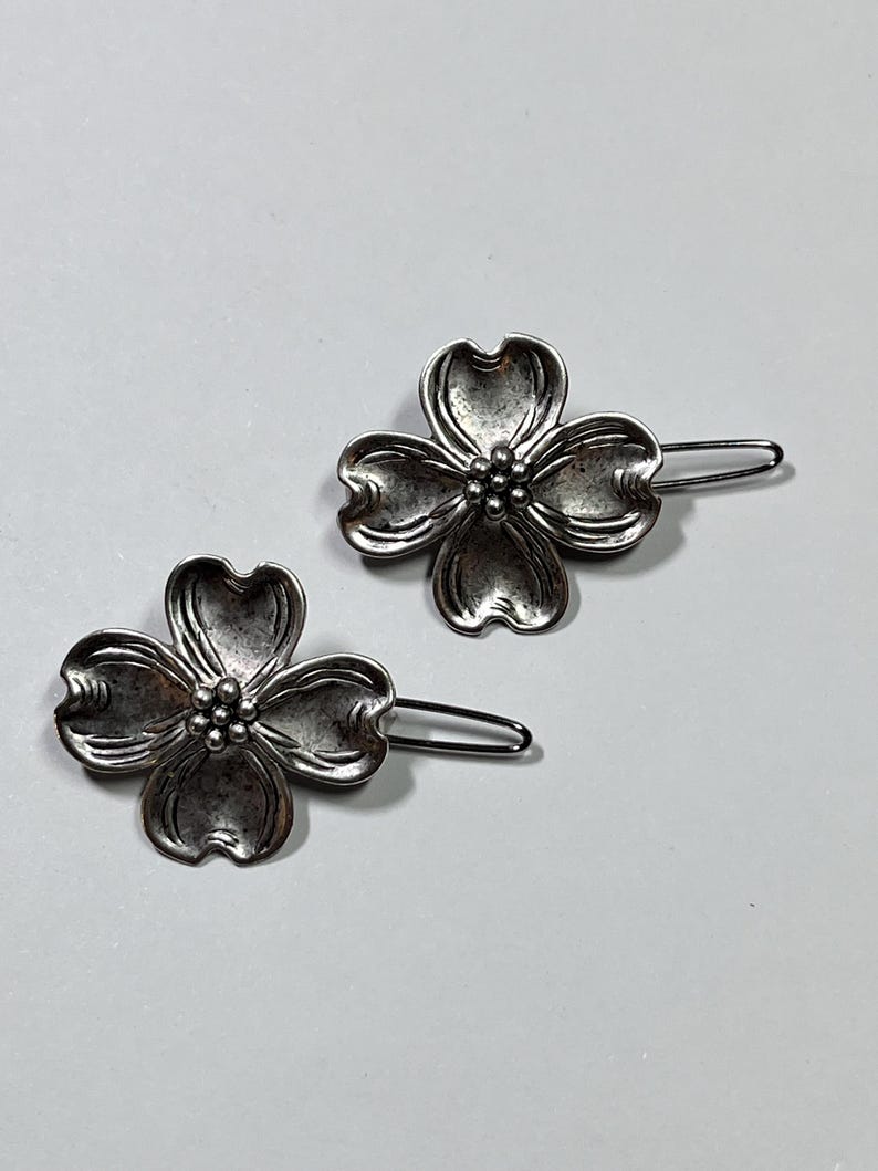 May include: Two silver-toned hair barrettes. Each barrette features a four-petal flower design with a cluster of small beads at the center. The barrettes are on a light gray background.