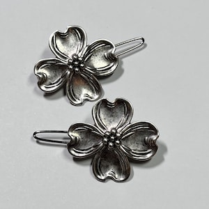 May include: Two silver-toned metal hair clips. Each clip features a flower design with four petals and a cluster of small beads at the center. The clips have a simple, curved bar for insertion into the hair.