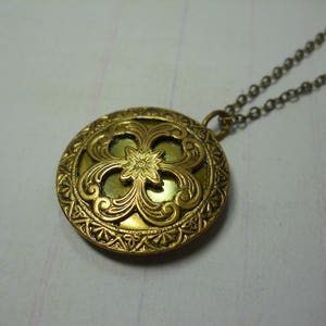 May include: A vintage-style gold-toned pendant necklace. The round pendant features an ornate floral design with a central flower and intricate detailing. The chain is a matching gold color, creating a cohesive and elegant piece of jewelry.