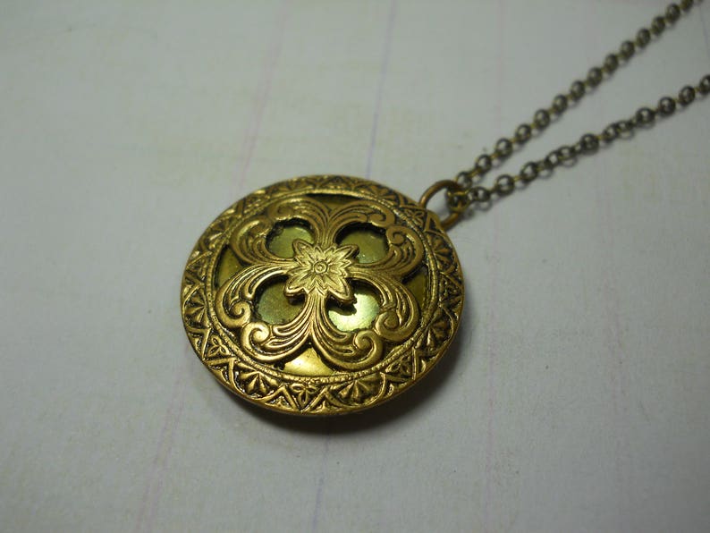 May include: A vintage-style gold-toned pendant necklace. The round pendant features an ornate floral design with a central flower and intricate detailing. The chain is a matching gold color, creating a cohesive and elegant piece of jewelry.