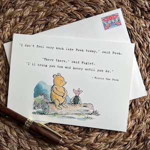 May include: Greeting card featuring Winnie the Pooh and Piglet, with a quote from the story. The illustration shows Pooh and Piglet on a log. The card is on a white envelope with a floral stamp, and a pen rests nearby.