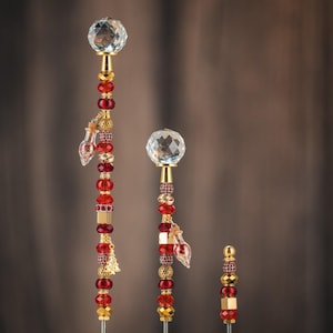 May include: Three decorative crystal and beaded wands with red and gold accents. The wands are different sizes and feature a crystal ball at the top.