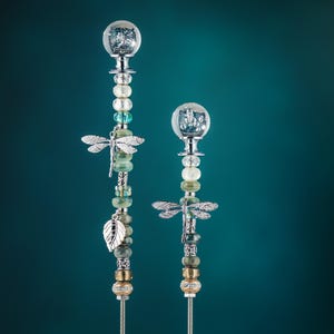May include: Two silver garden stakes with glass orbs and dragonfly accents. The stakes are decorated with beads and other embellishments.