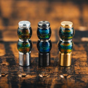 Op de afbeelding: Drie decoratieve flessenstoppers met iriserende glazen kralen. De stoppers zijn gemaakt van zilver, zwart en goud metaal.