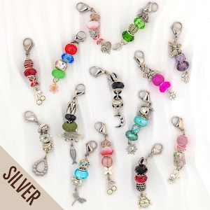 May include: A collection of twelve silver-toned metal charms featuring lobster claw clasps. Each charm is decorated with various colorful beads, including glass, textured, and patterned spheres, alongside small metal pendants shaped like butterflies, flowers, fish, moons, and insects.