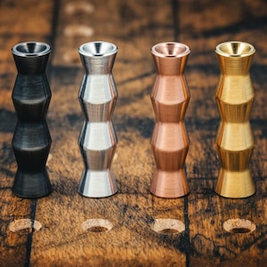 May include: Four metal beads in a row, each with a unique finish. The first is black, the second silver, the third copper, and the fourth gold. Each bead has a cylindrical shape with a flared top and bottom, and a series of stacked, angled sections.