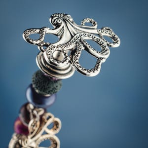 May include: A silver octopus charm with detailed tentacles, attached to a beaded bracelet with purple, green, and pink beads.