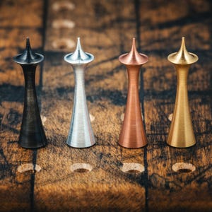 May include: Four decorative metal objects with a conical top and a flared base. The objects are in black, silver, copper, and gold colors. They are arranged on a wooden surface with circular indentations.