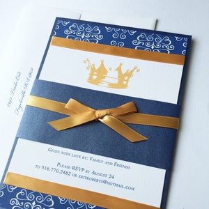 Op de afbeelding: Een blauwe en gouden uitnodiging met een kroonontwerp. De uitnodiging heeft een gouden lint eromheen gebonden. De tekst op de uitnodiging luidt "Given with love by: Family and Friends. Please RSVP by August 24 to 516.770.2482 or eritroberts@hotmail.com"
