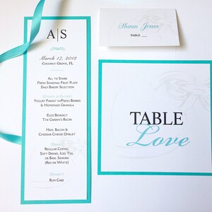 May include: A turquoise and white wedding table card with the text "Table Love" in black and turquoise lettering. The card has a decorative design in the upper right corner.