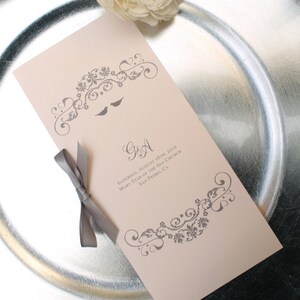 May include: A light pink wedding program with gray floral designs and the text "GA" in a script font. The date, "Saturday, August 18th, 2012", is printed below the initials. The text "Mary Star of the Sea Church" and "San Pedro, CA" are printed below the date.