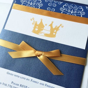 Op de afbeelding: Een marineblauwe uitnodiging met een gouden lint en strik. De uitnodiging heeft een gouden kroonontwerp en de tekst "Given with love by: Family and Friends. Please RSVP by August 24 to 516.770.2482 or eritroberts@hotmail.com"