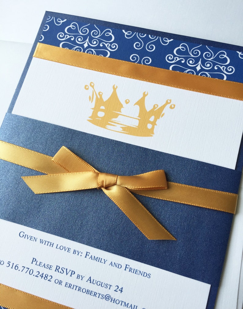 Op de afbeelding: Een marineblauwe uitnodiging met een gouden lint en strik. De uitnodiging heeft een gouden kroonontwerp en de tekst "Given with love by: Family and Friends. Please RSVP by August 24 to 516.770.2482 or eritroberts@hotmail.com"