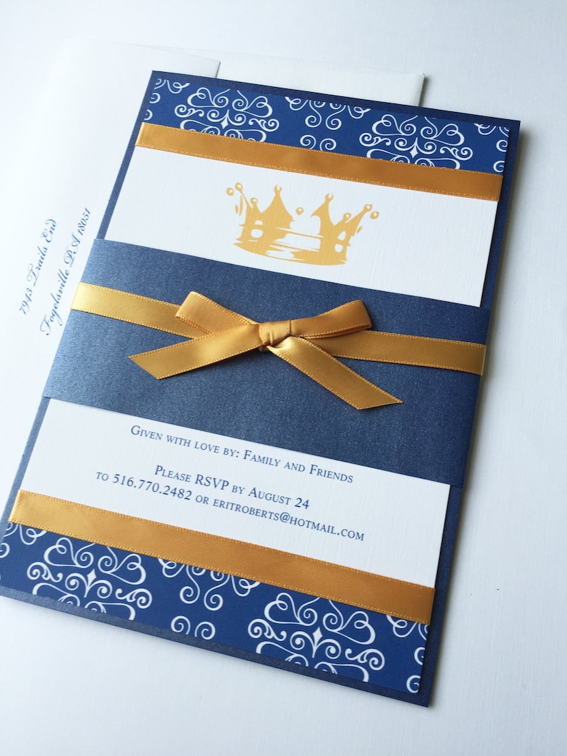 Op de afbeelding: Een blauwe en gouden uitnodiging met een kroonontwerp. De uitnodiging heeft een gouden lint eromheen gebonden. De tekst op de uitnodiging luidt "Given with love by: Family and Friends. Please RSVP by August 24 to 516.770.2482 or eritroberts@hotmail.com"