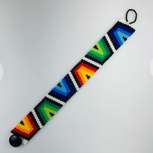 May include: A colorful beaded bracelet with a geometric pattern in shades of red, orange, yellow, green, blue, and black. The bracelet has a black button clasp.