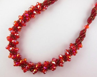 May include: A red beaded necklace with a spiral design. The beads are faceted and have a slight iridescent sheen.